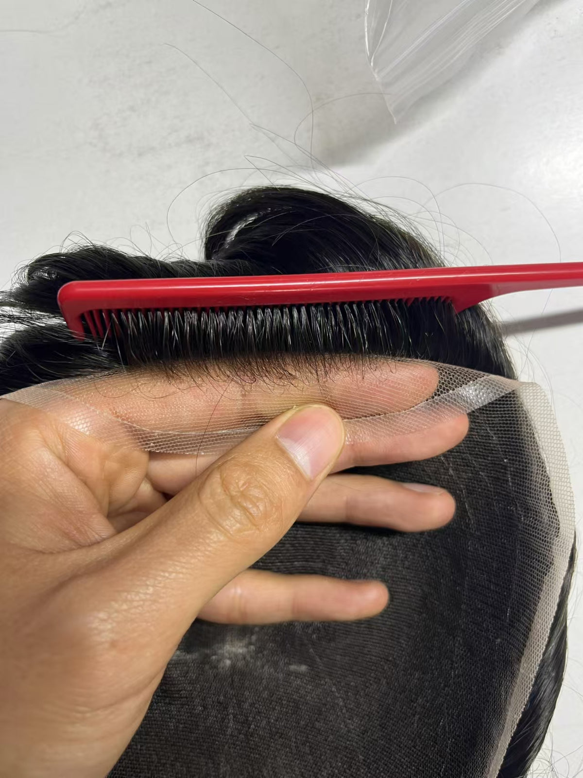 French lace stretched between fingers showing transparency with red comb and baby hairs