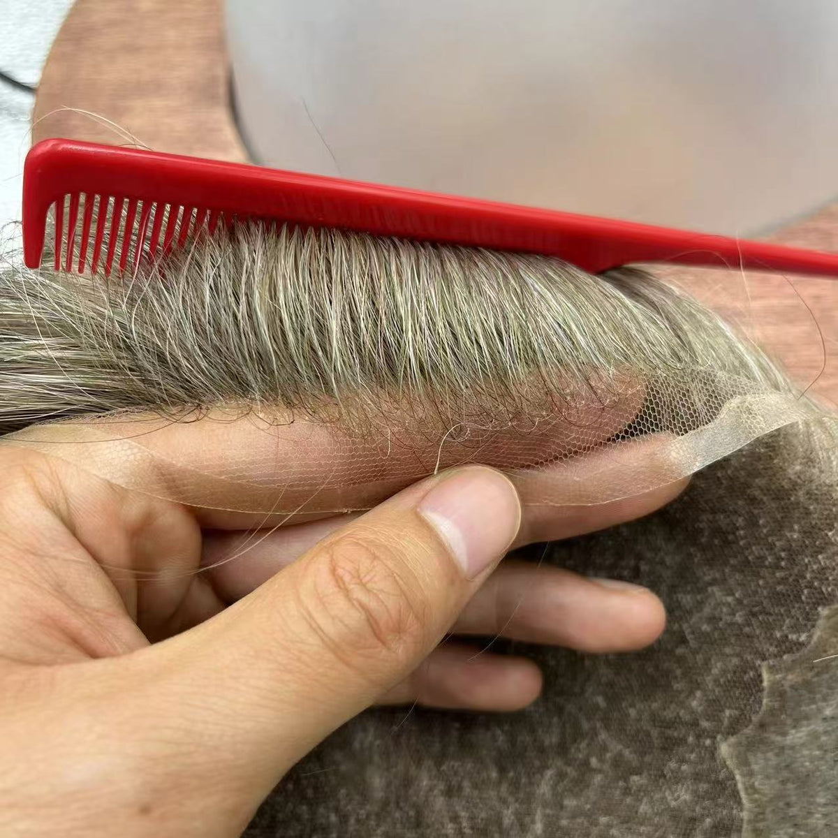Hand holding fine lace with gray-silver hair, red comb showing hand-tied density