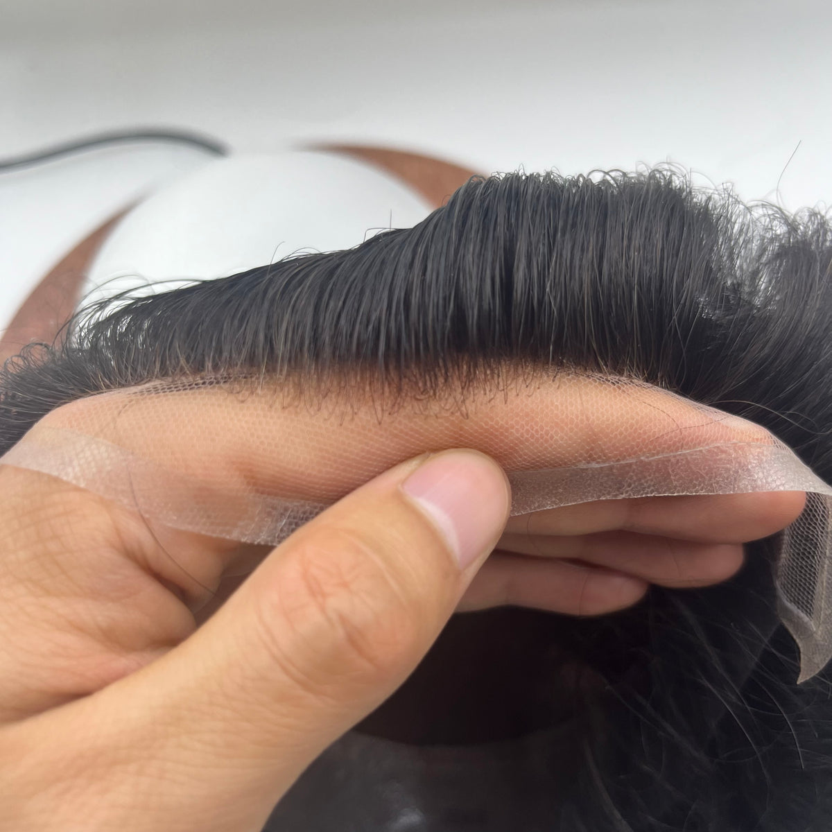 Fine French lace held between fingers showing hand-tied baby hairs at the hairline edge