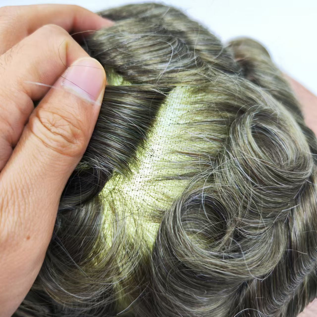 Hand parting hair to reveal fine monofilament base in gray-silver for natural scalp effect