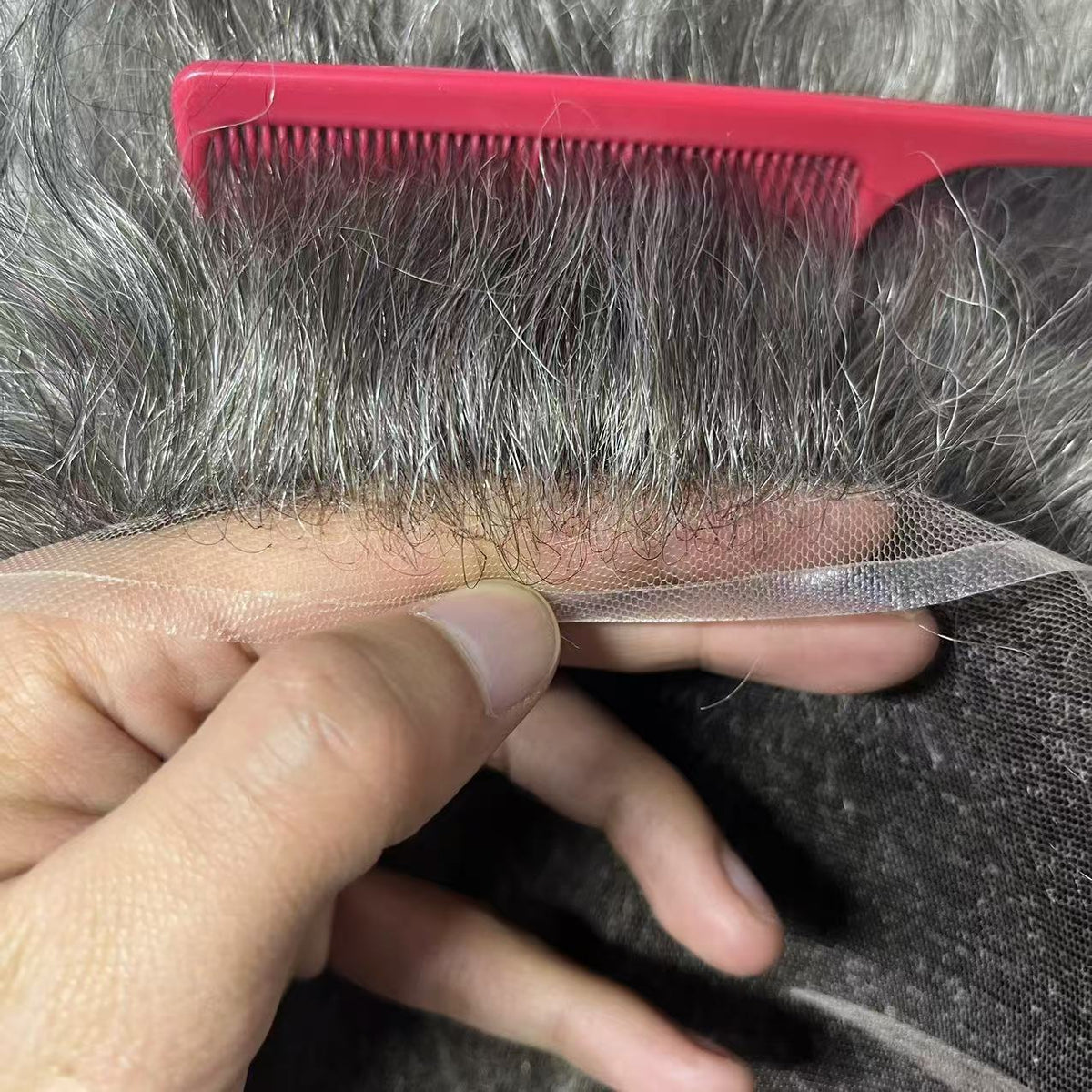 Hand holding Swiss lace front with pink comb showing transparent mesh and gray hairline