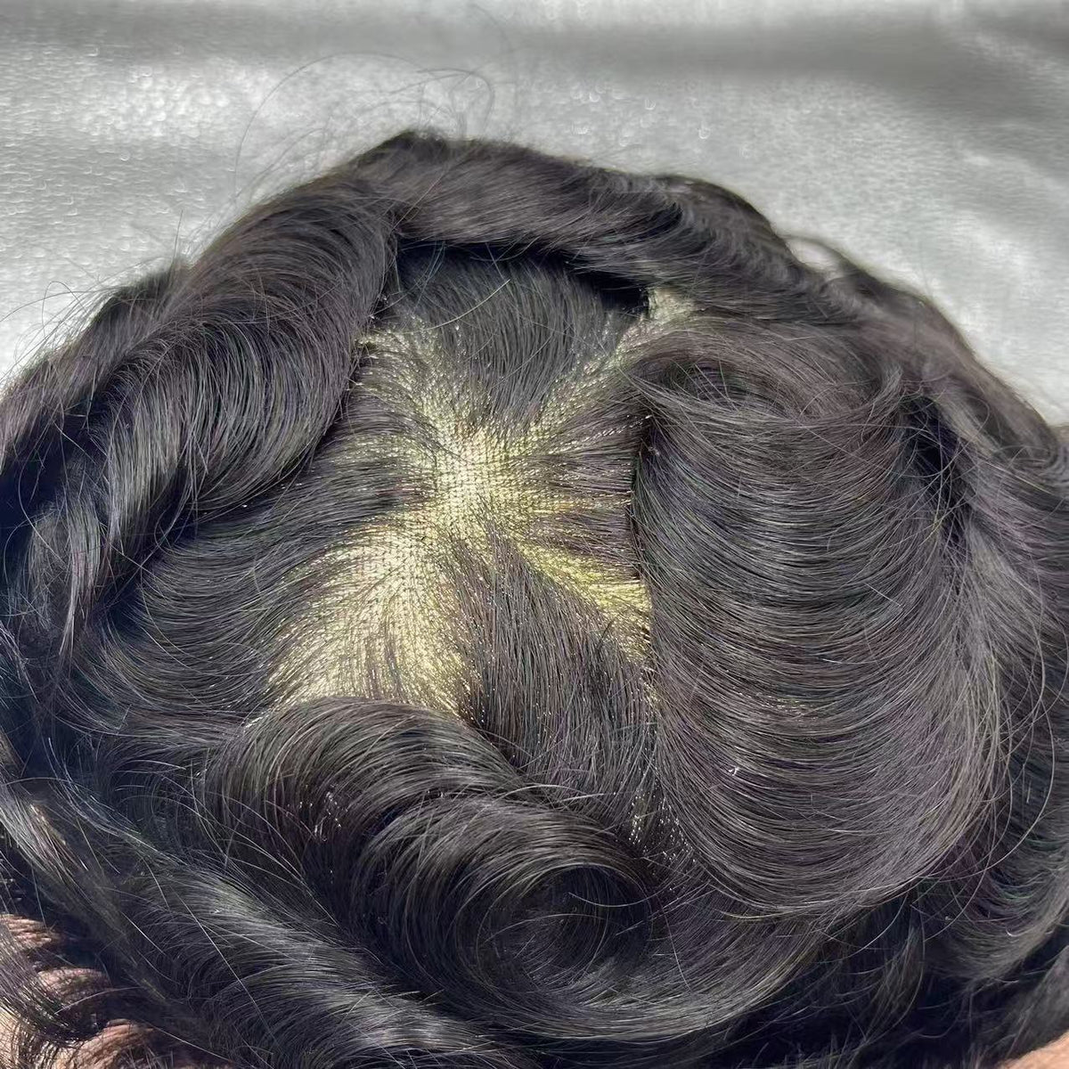 Parted crown showing fine mesh base between wavy dark hair for natural scalp effect